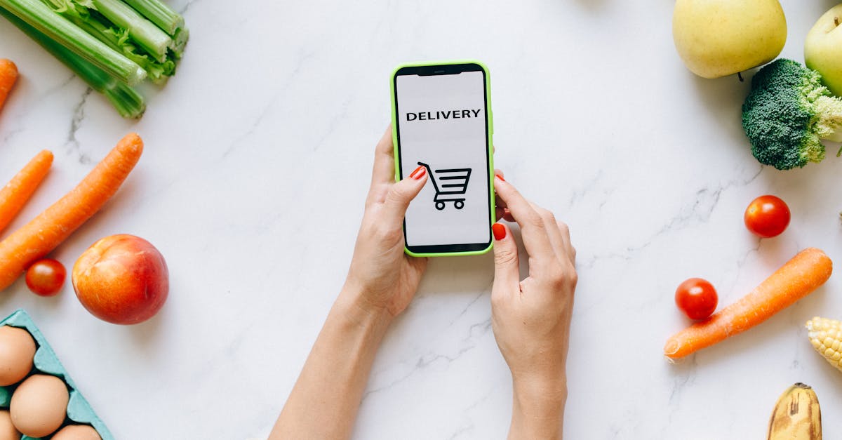 A person using a smartphone for grocery delivery surrounded by fresh fruits and vegetables.
