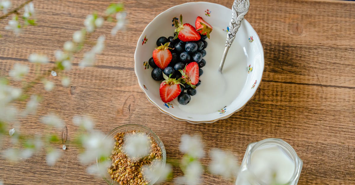 A bowl of fresh strawberries, blueberries with yogurt on a wooden table, viewed from above.