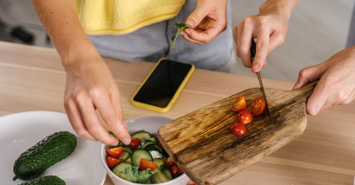A close-up shot of hands cutting fresh vegetables for a salad on a wooden chopping board indoors.
