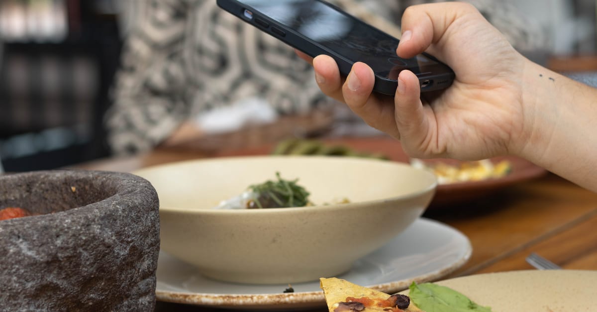 A person takes a photo of their meal using a smartphone at a restaurant table.