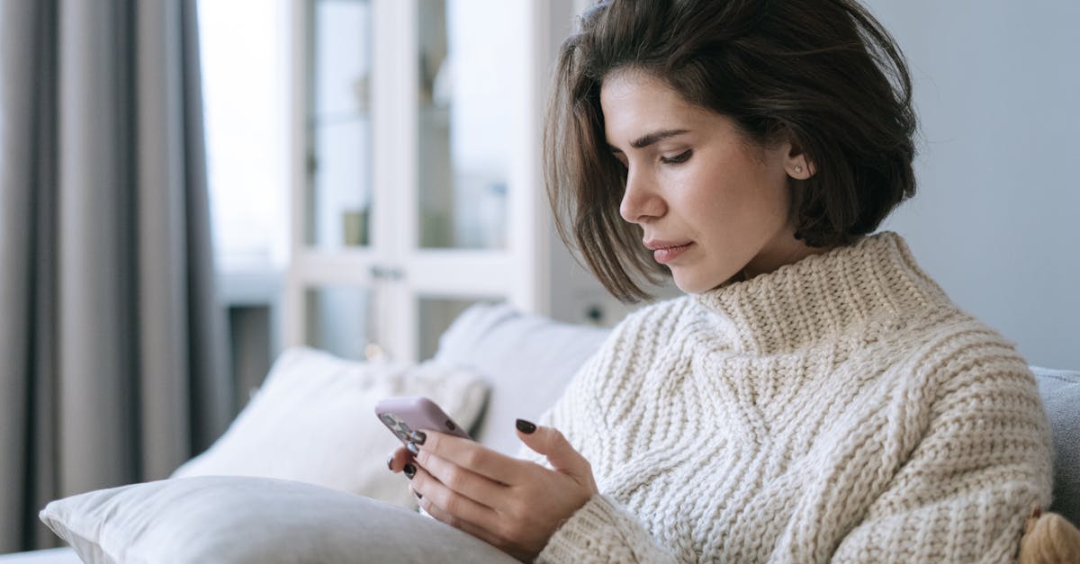 Woman in knitted sweater using smartphone on a cozy sofa indoors.