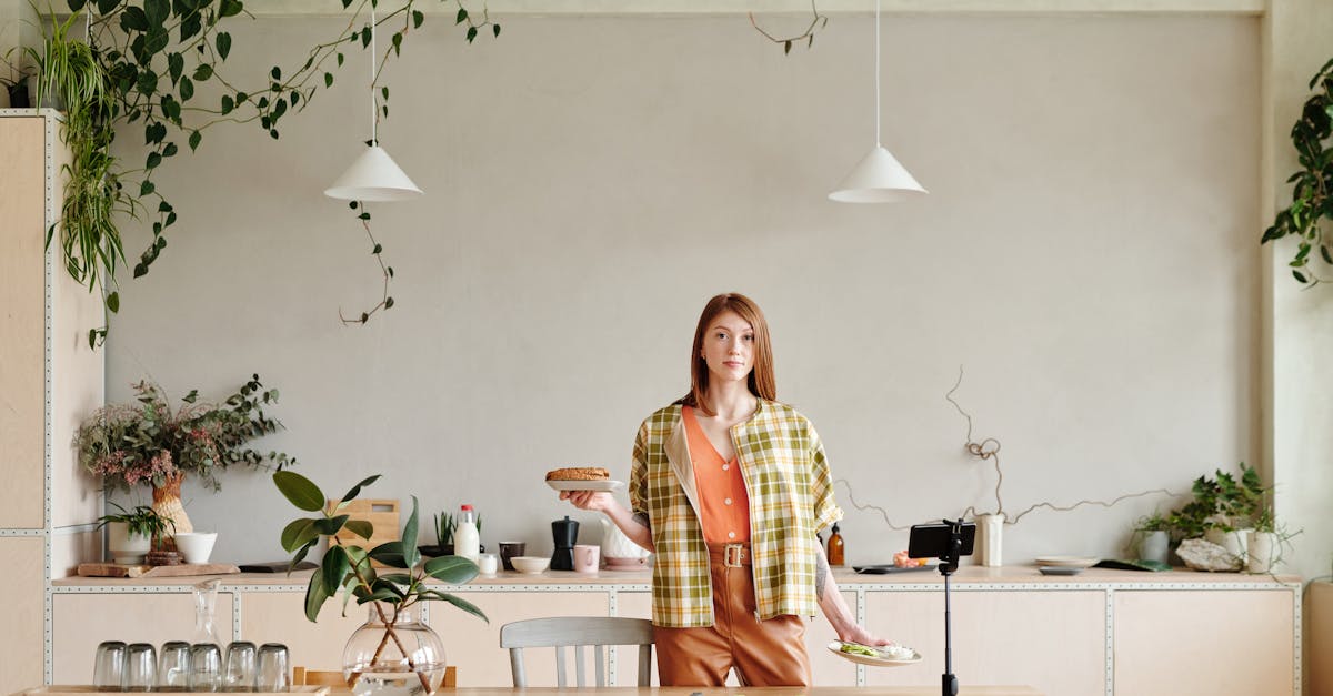 Woman in a modern kitchen setting up food for a vlog with a smartphone and tripod.
