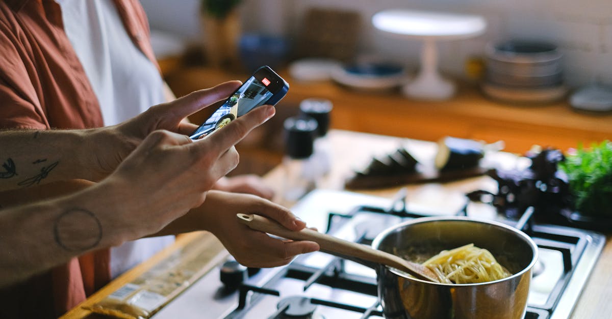 A couple cooks spaghetti while capturing the moment on a phone, showcasing cooking and photography harmony.
