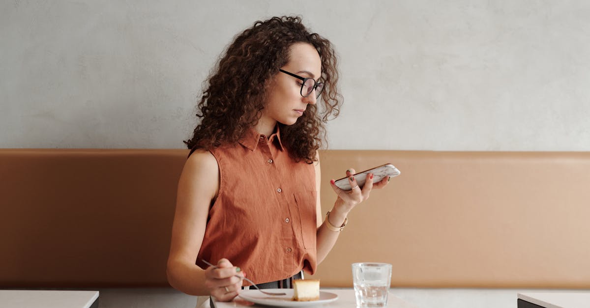 Woman with curly hair multitasks with smartphone and food in a cafe setting.
