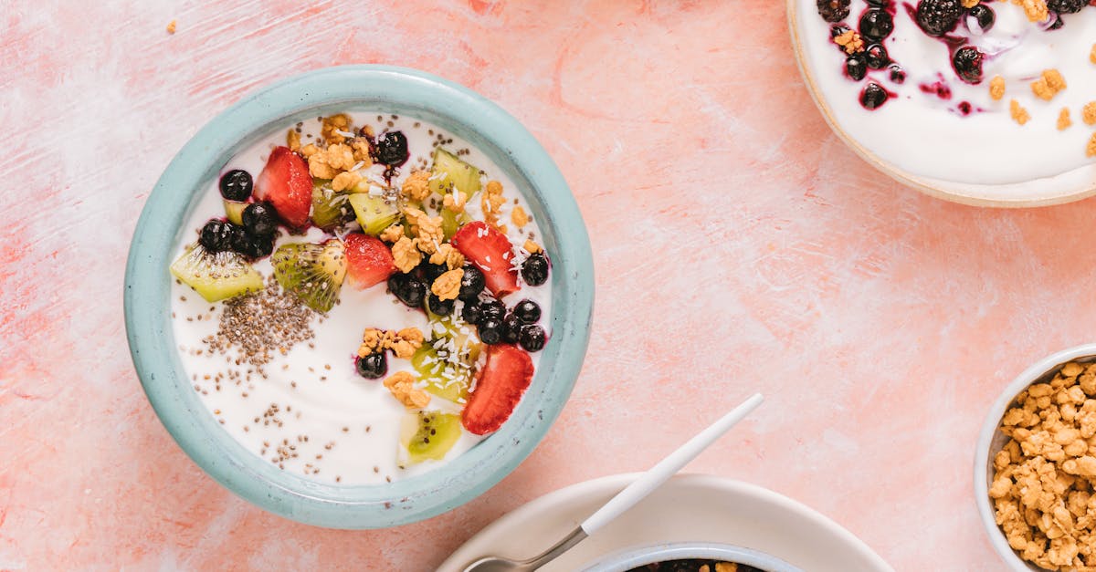 Top view of colorful yogurt bowls topped with fresh berries and granola on a rustic background.