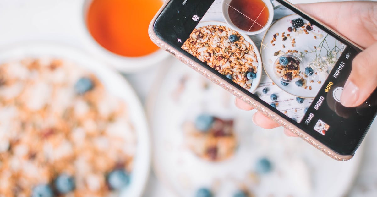 A smartphone capturing a healthy breakfast bowl with blueberries and tea.