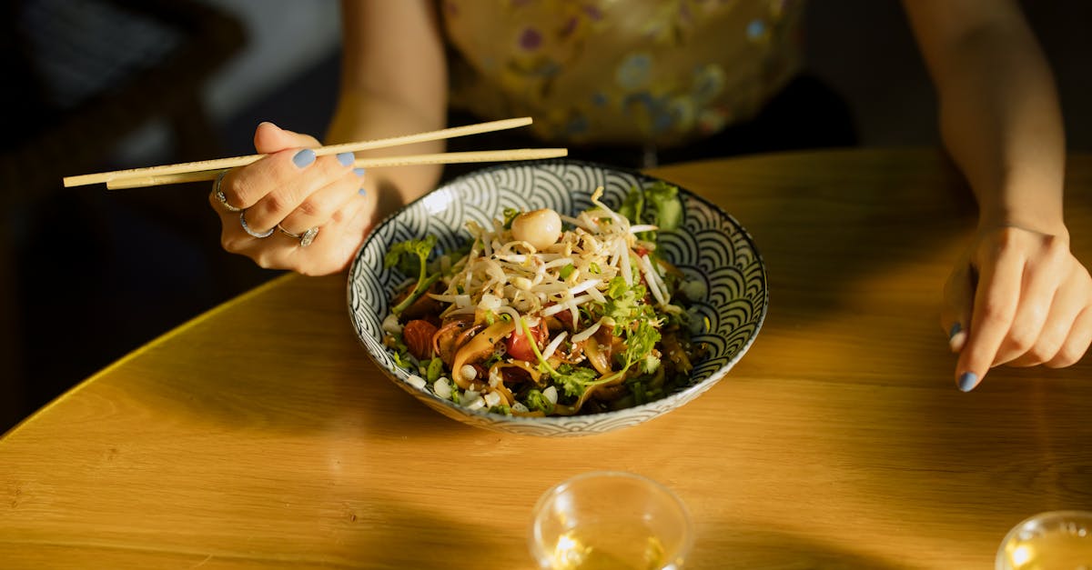 Individual savoring Asian fusion salad with chopsticks at a cozy indoor setting.